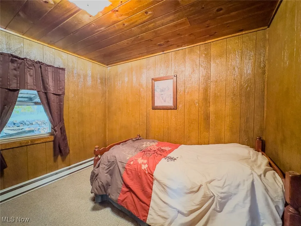 Carpeted bedroom with wooden walls, baseboard heating, and wooden ceiling