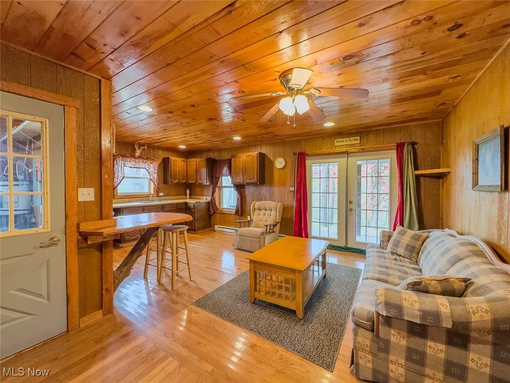 Living room featuring wood walls, wood ceiling, light wood-type flooring, healthy amount of natural light, and ceiling fan