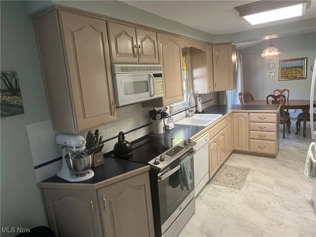 Kitchen with dark countertops, white appliances, a peninsula, light brown cabinetry, and tasteful backsplash