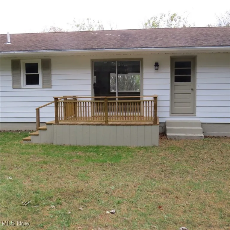Rear view of house featuring a yard, roof with shingles, and a deck