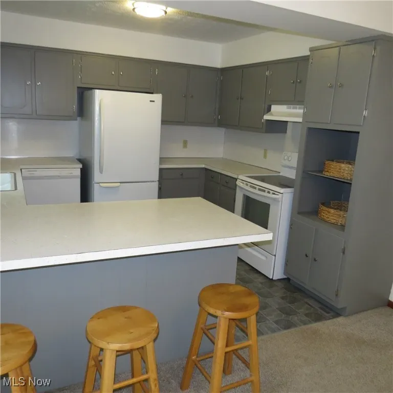 Kitchen featuring white appliances, light countertops, gray cabinets, a kitchen breakfast bar, and a peninsula