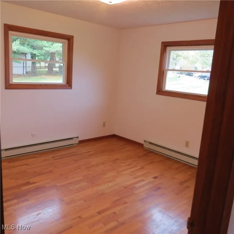 Unfurnished room with a baseboard heating unit and light wood-type flooring