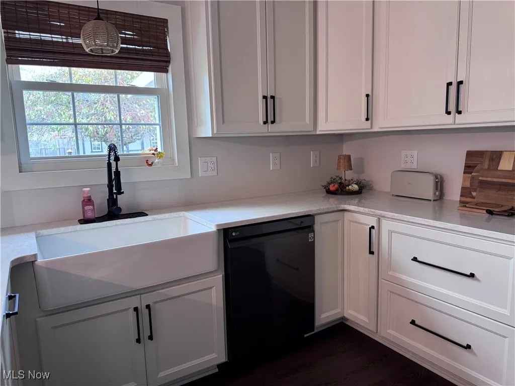 Kitchen featuring white cabinets, dishwasher, light stone countertops, and hanging light fixtures
