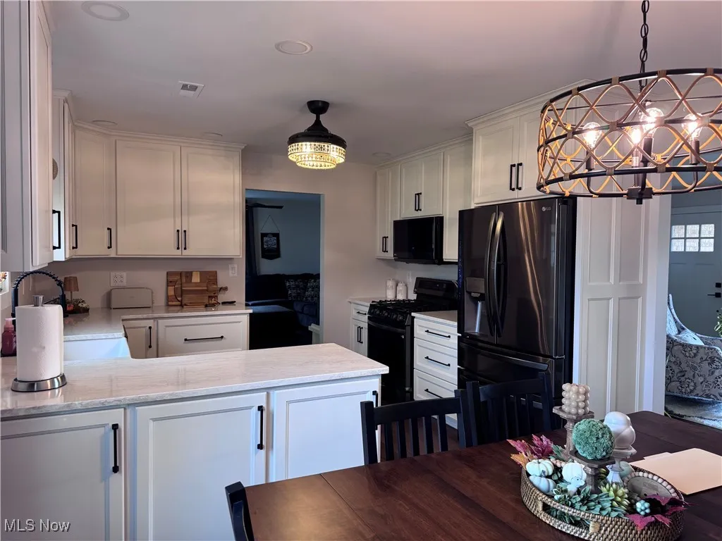 Kitchen with a chandelier, black appliances, light stone counters, and white cabinetry