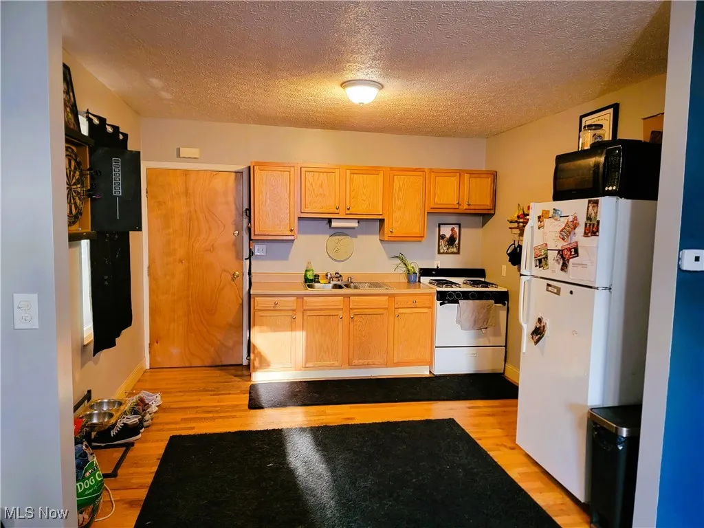 Kitchen with white appliances, light countertops, light wood-type flooring, a textured ceiling, and light brown cabinets