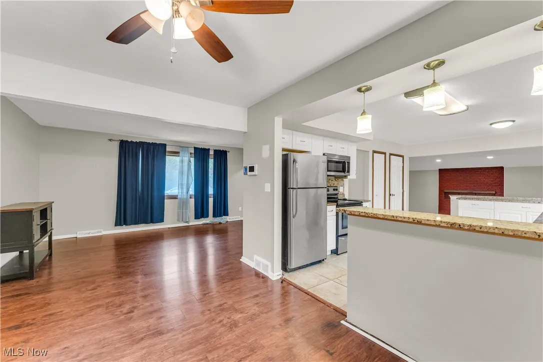Kitchen featuring hanging light fixtures, appliances with stainless steel finishes, white cabinetry, light wood-type flooring, and light stone countertops