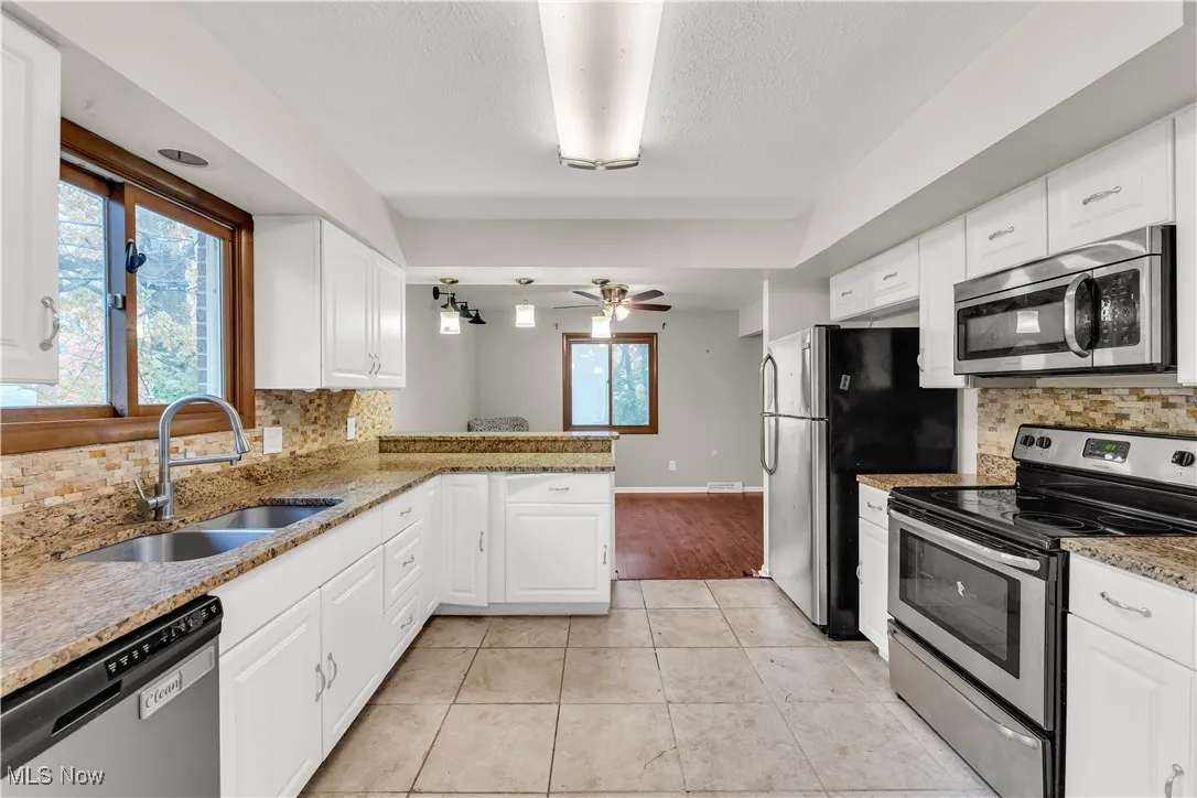 Kitchen featuring decorative backsplash, appliances with stainless steel finishes, light stone counters, white cabinets, and a textured ceiling
