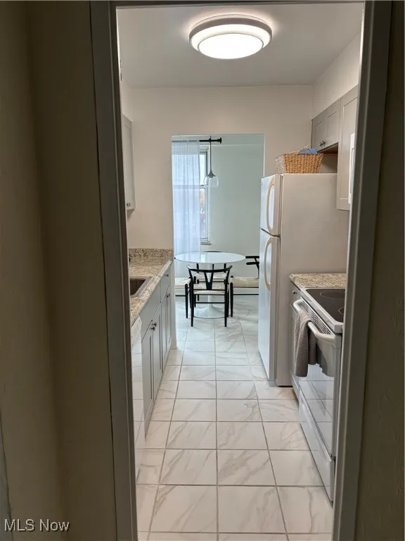 Kitchen with stove, gray cabinetry, light stone counters, and white refrigerator