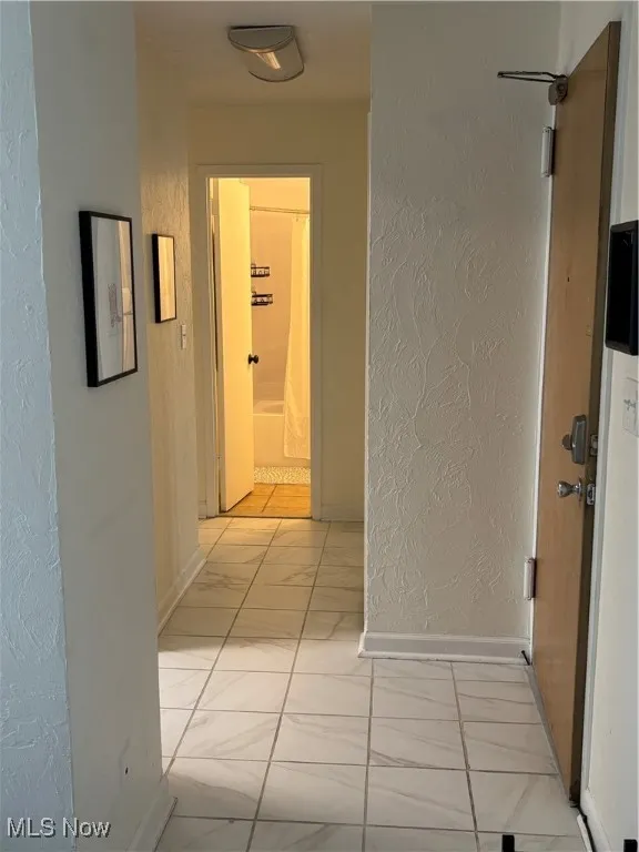 Hallway featuring a textured wall and baseboards
