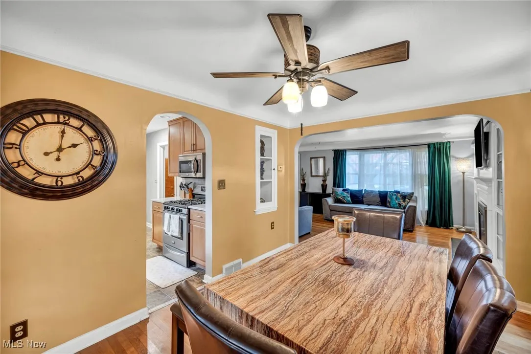 Dining space with arched walkways, wood finished floors, ornamental molding, a glass covered fireplace, and a ceiling fan
