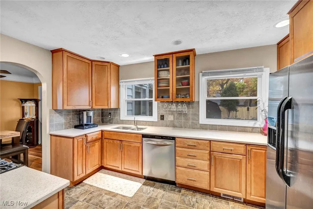Kitchen with stainless steel appliances, backsplash, arched walkways, glass insert cabinets, and recessed lighting