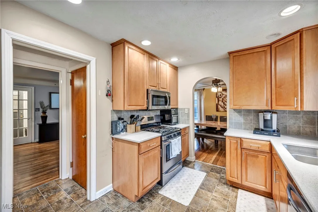 Kitchen with stainless steel appliances, a ceiling fan, arched walkways, tasteful backsplash, and light stone countertops