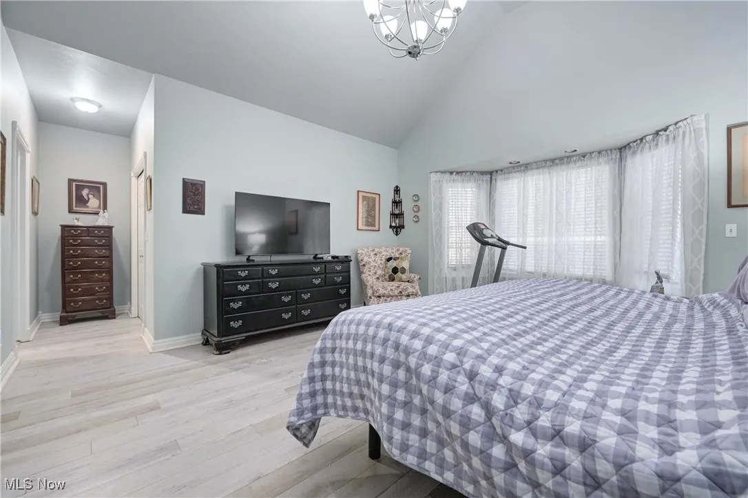 Bedroom with a chandelier, wood finished floors, and high vaulted ceiling