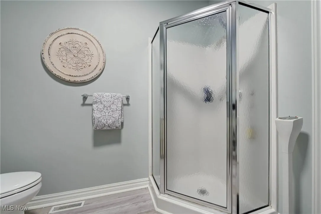 Full bath with light wood finished floors and a shower stall