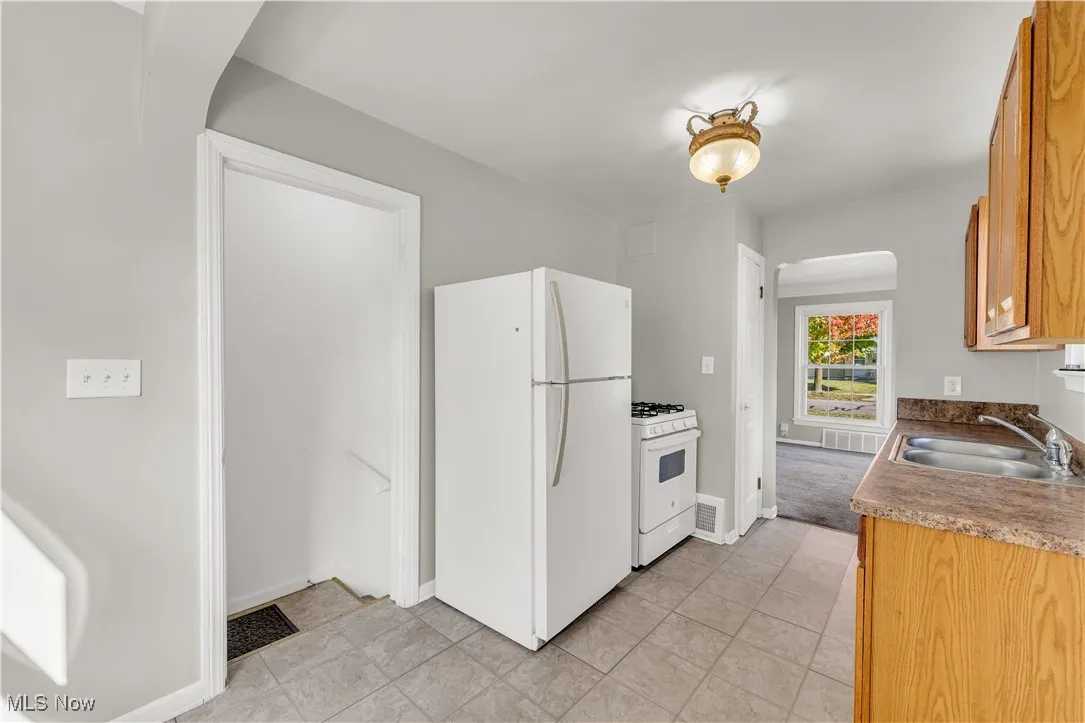 Kitchen featuring white appliances, arched walkways, light tile patterned floors, and brown cabinets