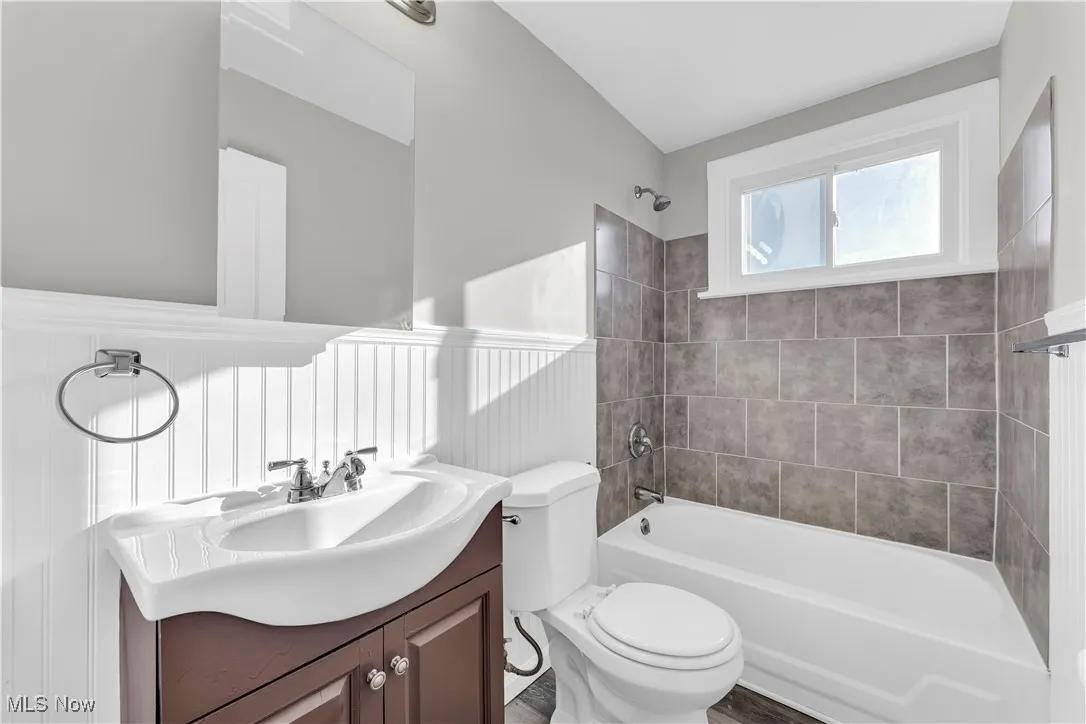 Bathroom with vanity, bathtub / shower combination, and a wainscoted wall