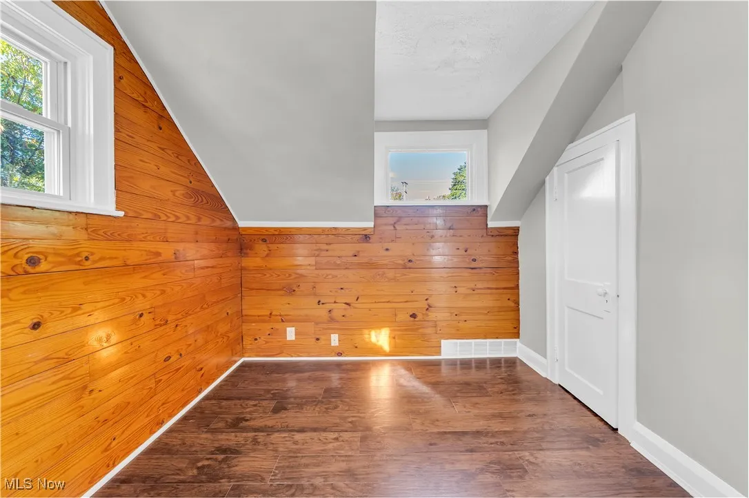 Additional living space with vaulted ceiling, wood finished floors, and wood walls