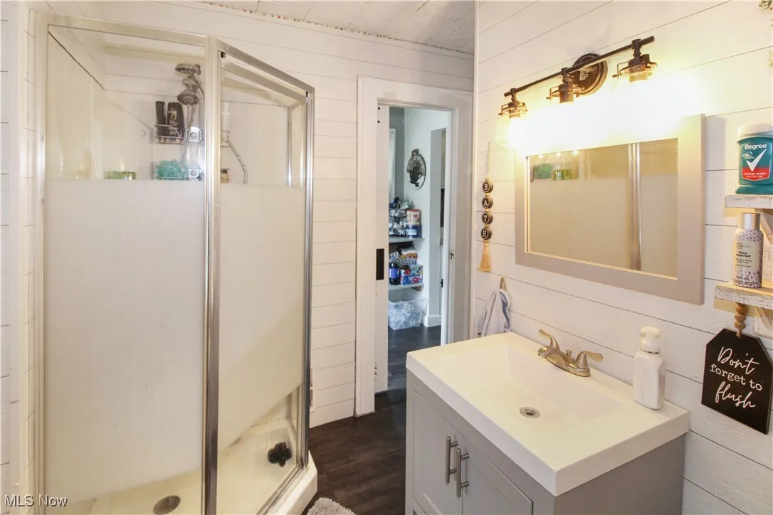 Bathroom with wooden walls, vanity, a stall shower, and dark wood-style floors