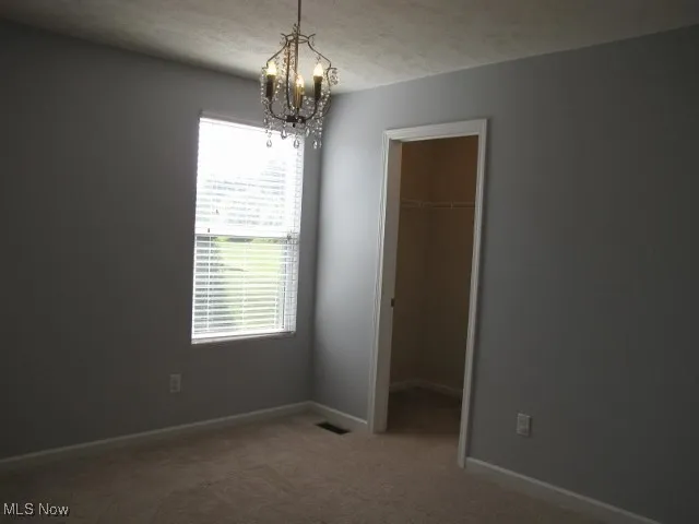 Back corner bedroom with light beige carpet and walk-in closet with light, chandelier as lighting!