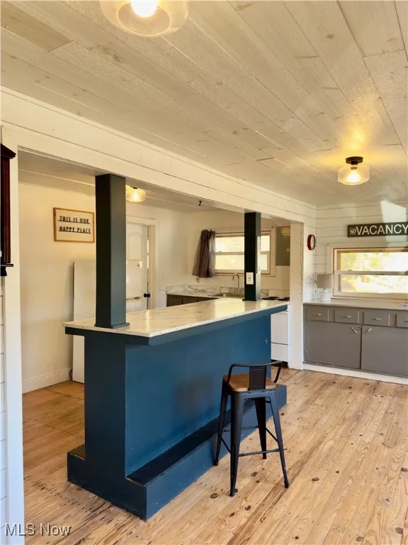 Kitchen featuring light wood-type flooring, wood ceiling, a kitchen bar, gray cabinets, and blue cabinets