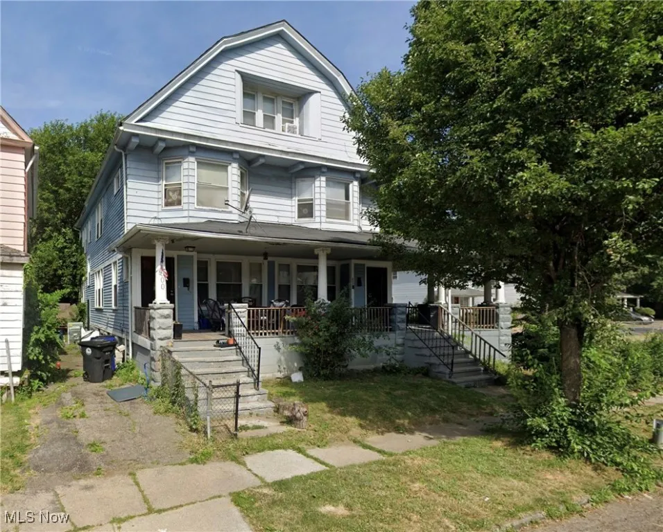 View of front facade with a gambrel roof, covered porch, a front lawn, and stairway