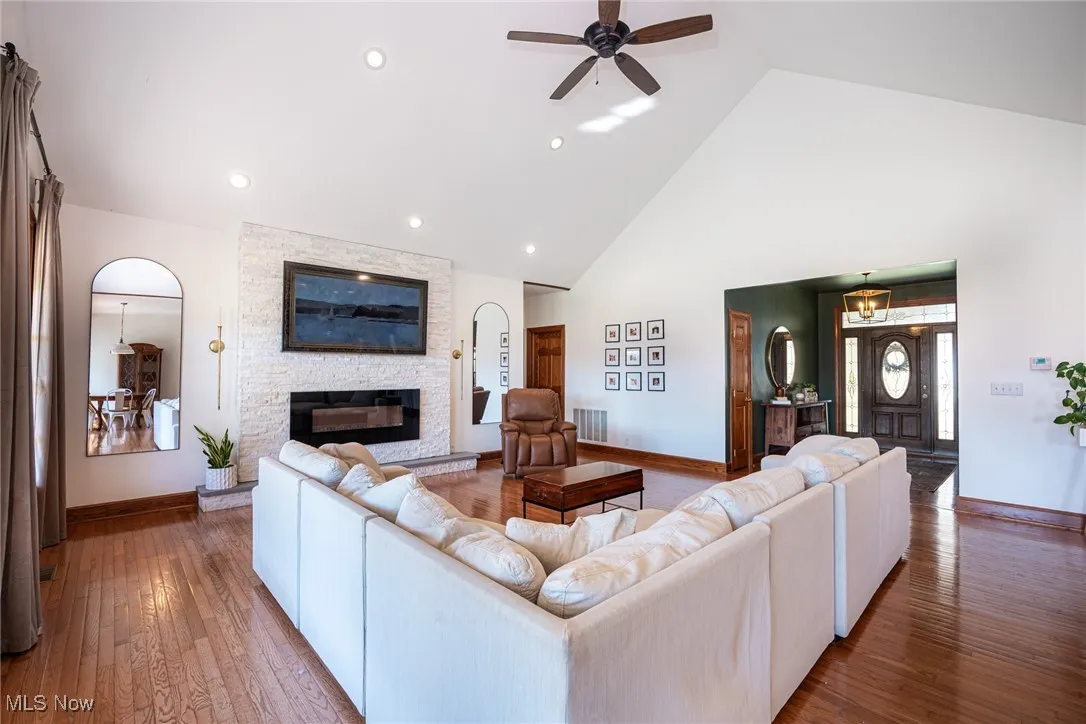 Living room featuring high vaulted ceiling, wood-type flooring, ceiling fan, and a fireplace