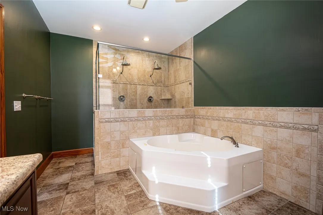 Full bath with a bath, tile walls, tiled shower, vanity, and recessed lighting