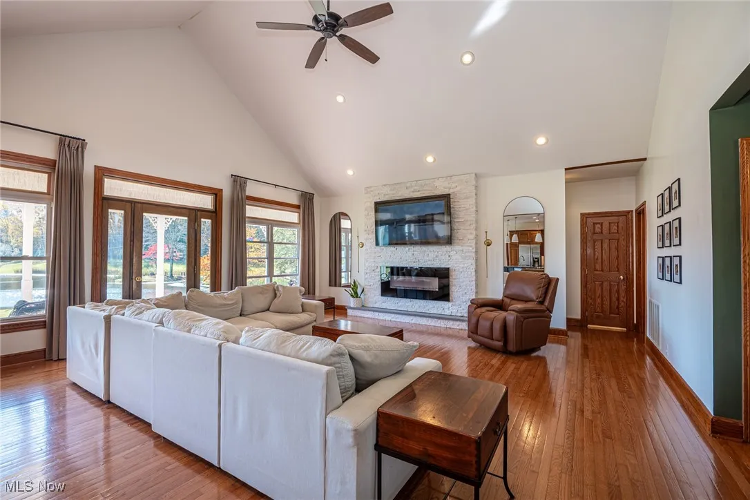 Living room with high vaulted ceiling, wood-type flooring, ceiling fan, recessed lighting, and a fireplace