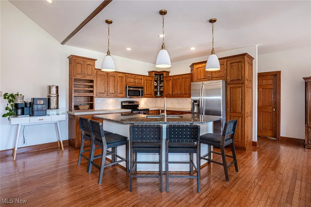 Kitchen featuring a kitchen bar, brown cabinets, decorative light fixtures, decorative backsplash, and a center island with sink