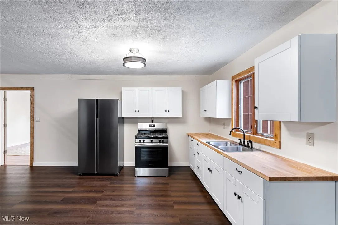 Kitchen with freestanding refrigerator, stainless steel gas range oven, white cabinets, wooden counters, and a textured ceiling