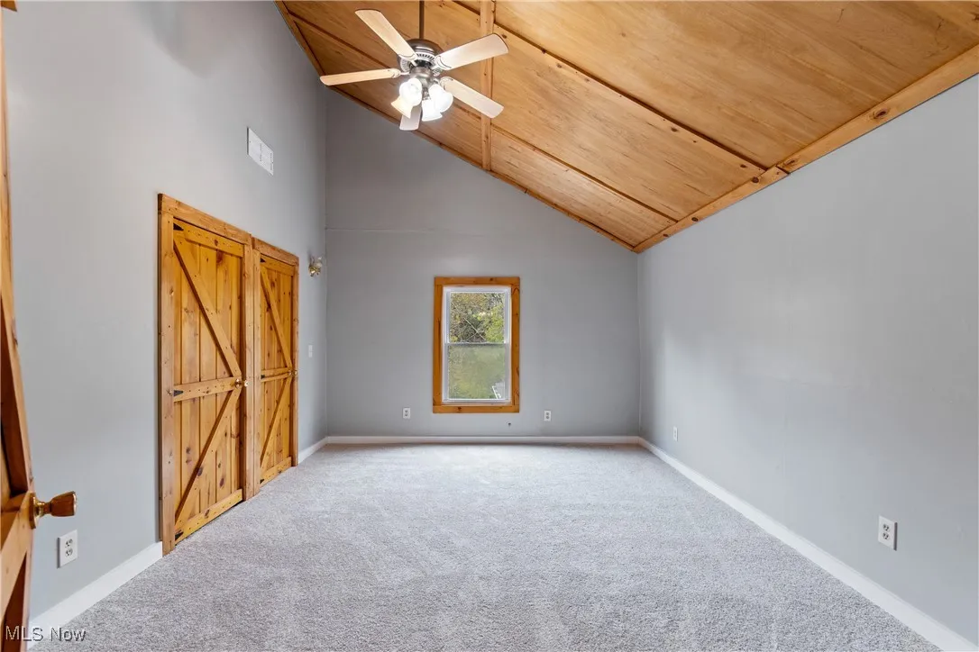 Unfurnished bedroom featuring high vaulted ceiling, carpet flooring, ceiling fan, and wooden ceiling