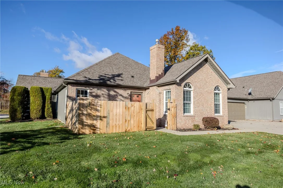 Rear view of house featuring a chimney, brick siding, a gate, and concrete driveway