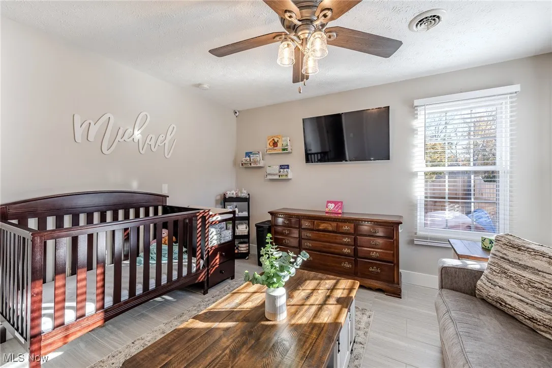 Bedroom featuring a nursery area, a textured ceiling, light wood-style floors, and ceiling fan