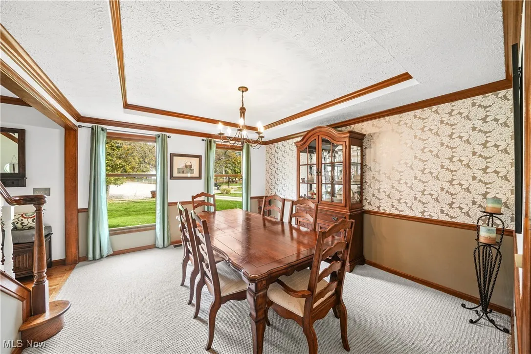 Dining space featuring a tray ceiling, a chandelier, ornamental molding, a textured ceiling, and carpet floors
