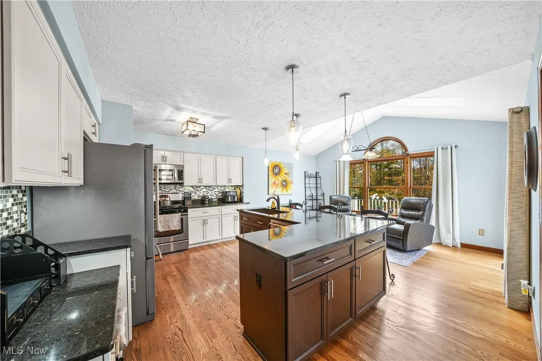 Kitchen featuring tasteful backsplash, light wood-style floors, dark stone counters, appliances with stainless steel finishes, and hanging light fixtures
