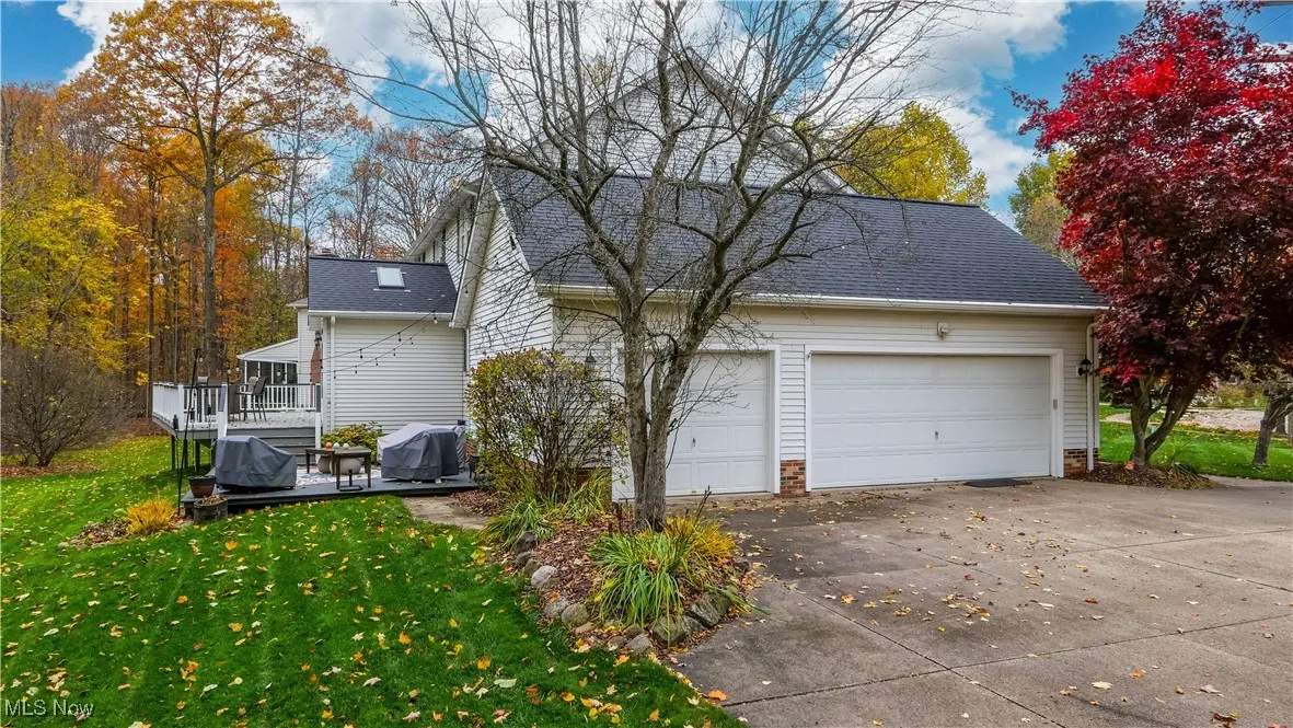 View of property exterior featuring a lawn, driveway, a wooden deck, and a shingled roof
