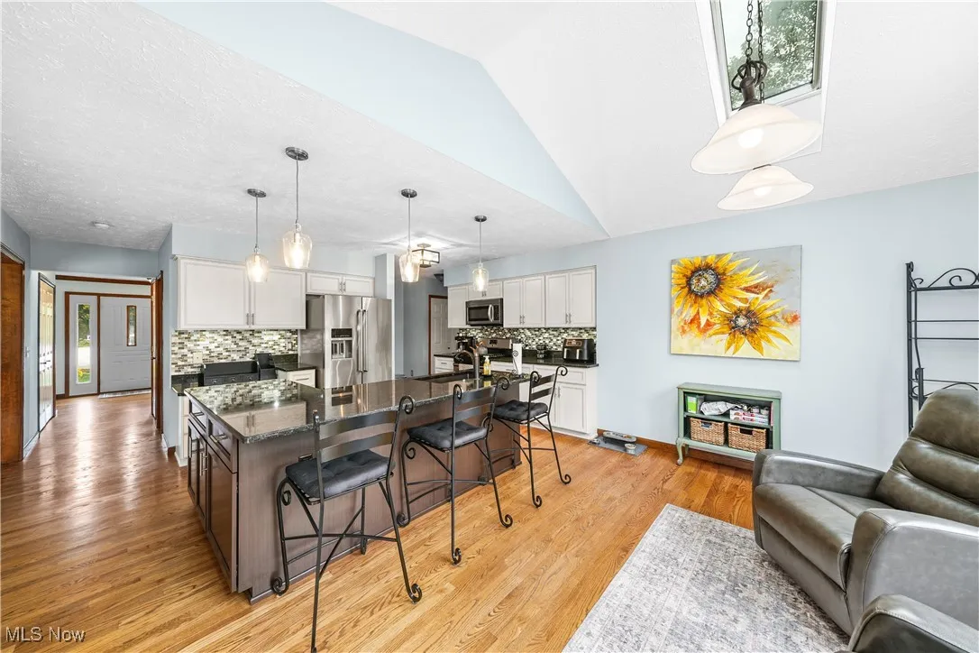 Kitchen with a kitchen bar, an island with sink, appliances with stainless steel finishes, white cabinets, and dark stone counters