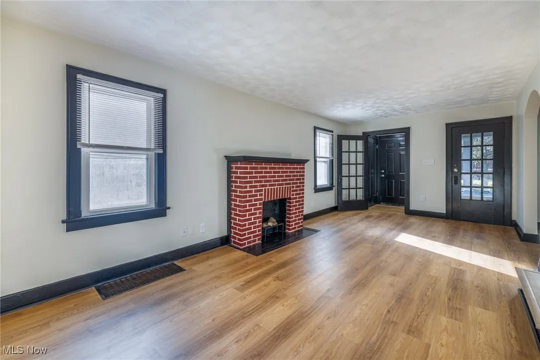 Unfurnished living room featuring plenty of natural light, a brick fireplace, light wood finished floors, a textured ceiling, and arched walkways