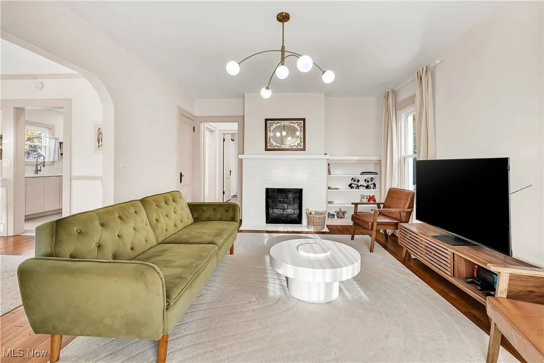 Living area with a brick fireplace, wood finished floors, arched walkways, and a chandelier