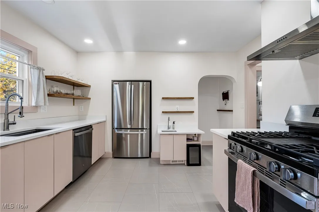 Kitchen with open shelves, stainless steel appliances, wall chimney exhaust hood, arched walkways, and light stone counters