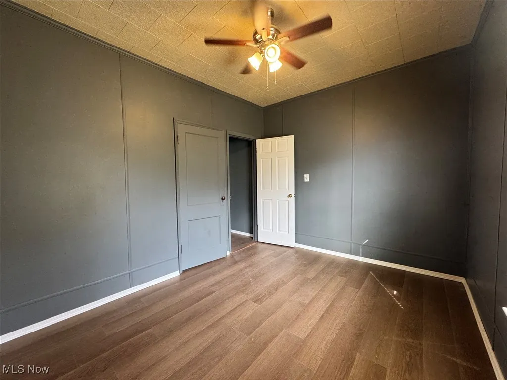 Unfurnished bedroom featuring wood finished floors, a decorative wall, and a ceiling fan