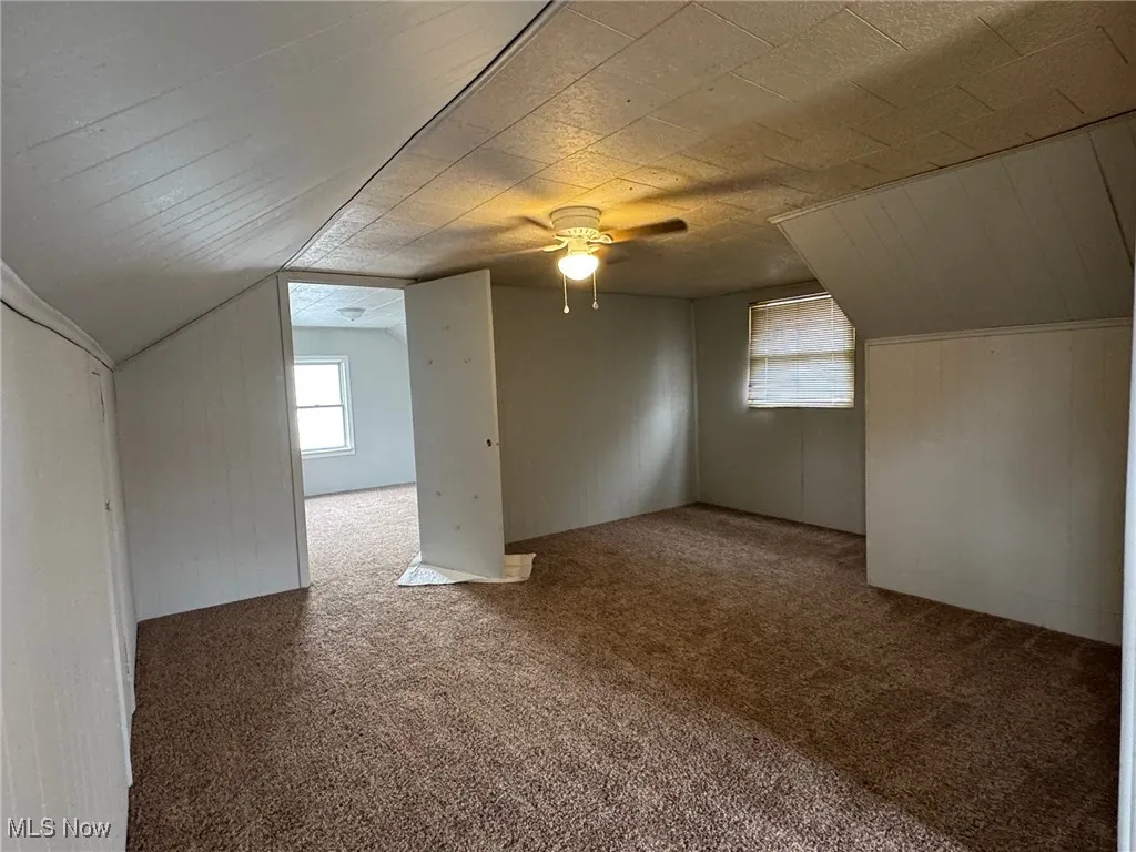 Bonus room with carpet, healthy amount of natural light, wood walls, and lofted ceiling