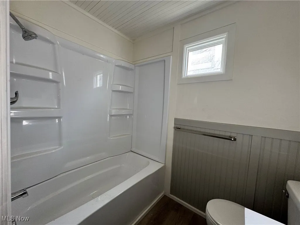 Full bath featuring dark wood-style flooring, bathtub / shower combination, and wainscoting