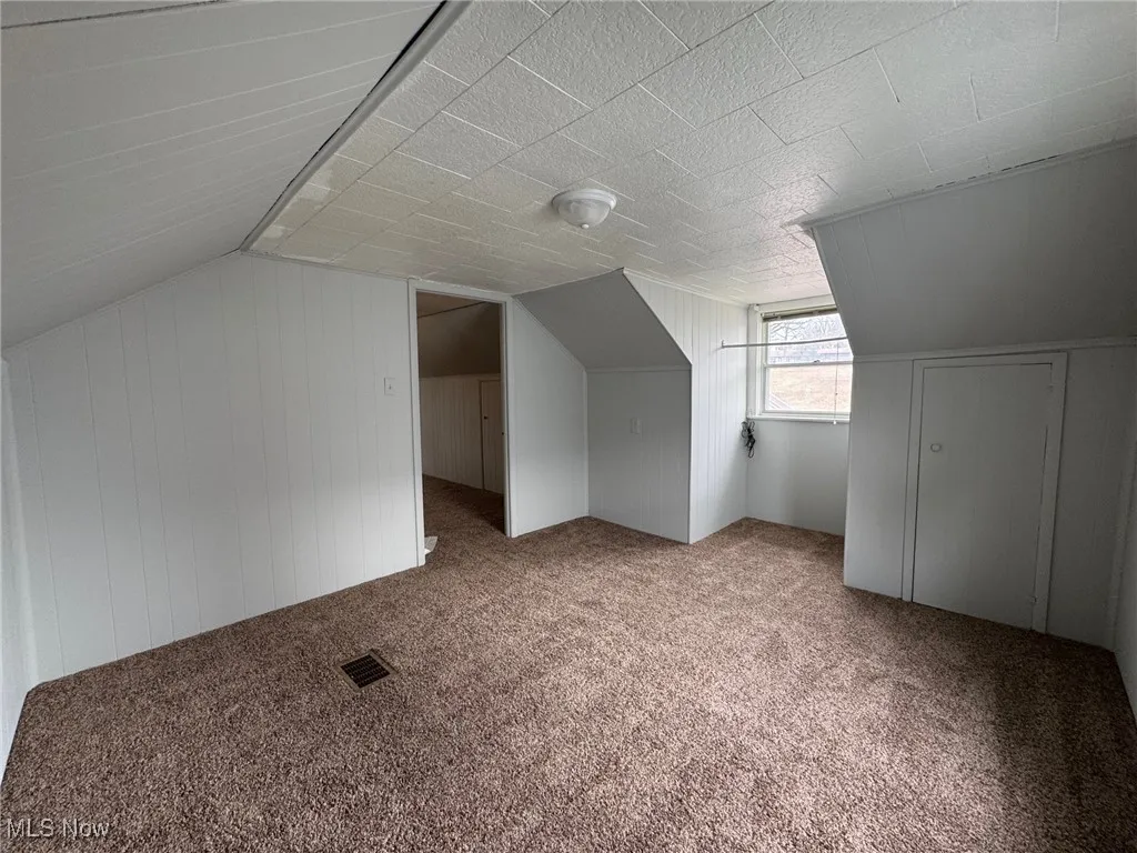 Bonus room with carpet, lofted ceiling, and wood walls