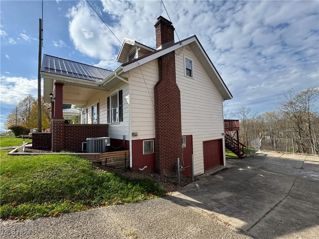 View of side of home with a metal roof, driveway, a garage, a chimney, and stairs