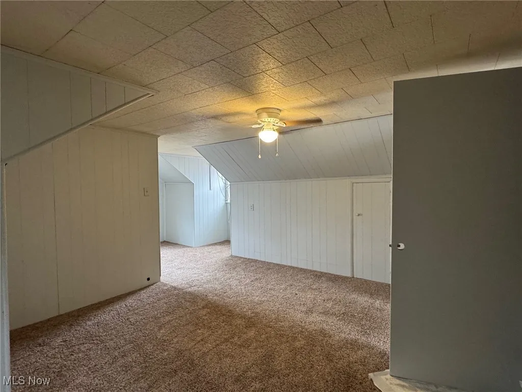 Additional living space with carpet flooring, lofted ceiling, wooden walls, and ceiling fan