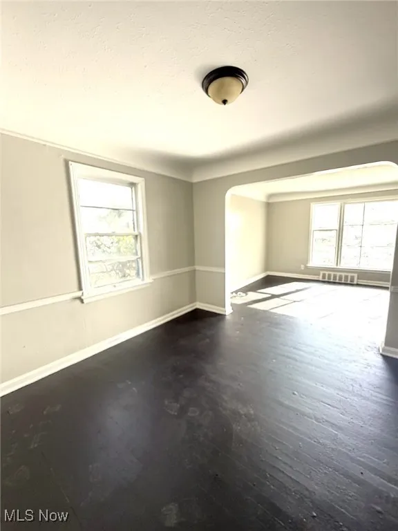 Spare room featuring arched walkways, dark wood-style flooring, healthy amount of natural light, and a textured ceiling