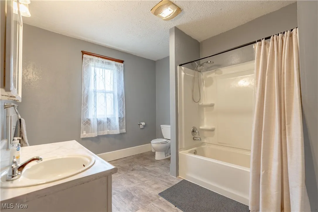 Full bathroom featuring vanity, a textured ceiling, and shower / bathtub combination with curtain