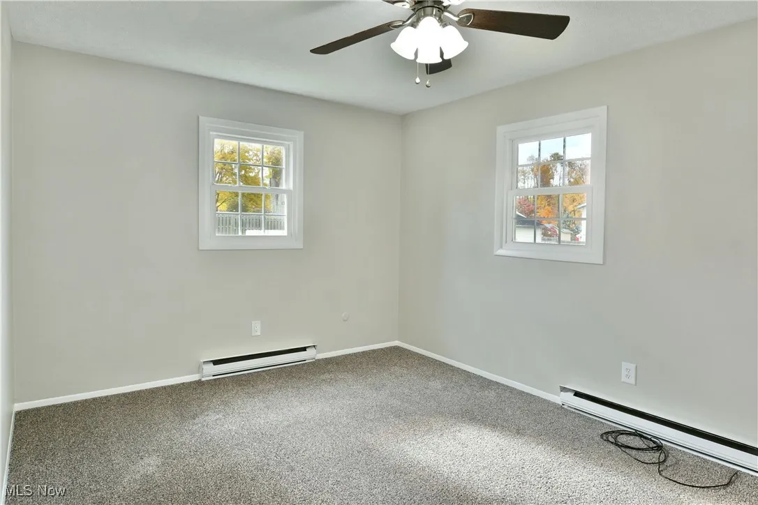Spare room with baseboard heating, carpet, a baseboard heating unit, and a ceiling fan