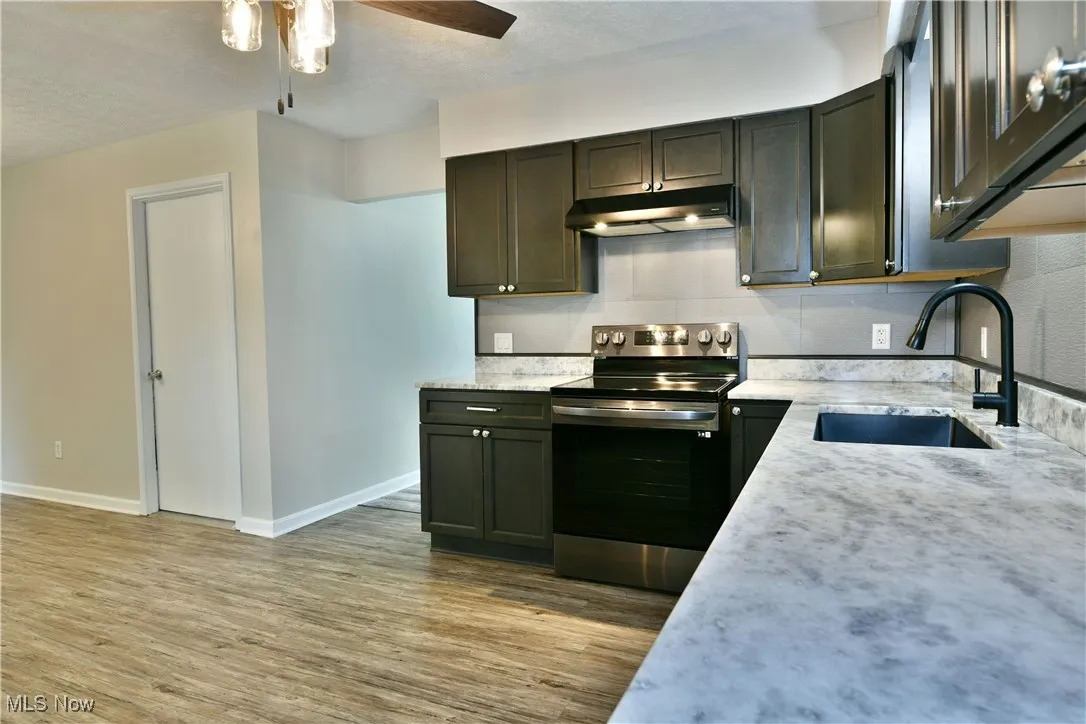 Kitchen with stainless steel electric range, light wood finished floors, under cabinet range hood, a textured ceiling, and a ceiling fan